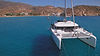 Aerial view from bow to stern, catamaran on right, child mid‑air jumping into crystal‑clear blue water, beautiful anchorage, Family Holiday sailing experience.