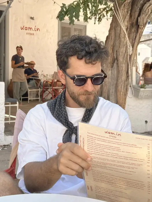 Man studying a menu at a traditional Greek taverna, anticipating a delicious meal on La Dolce Vita sailing experience.