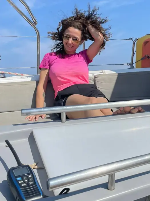 Woman on windward side with wind‑blown hair, holding it back, fun sailing moment, Salty Fundamentals.
