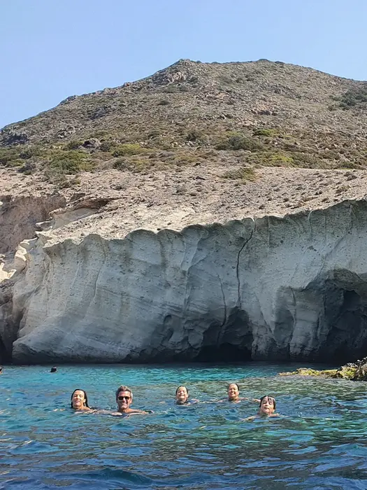 Family of five floating in crystal water, smiling at camera, unforgettable Family Holiday memory in Greece.