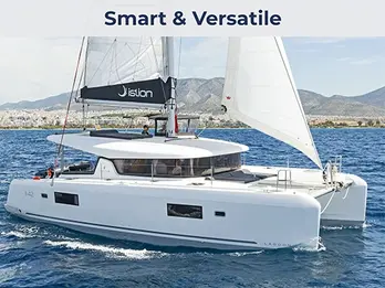 Aerial side view of a Lagoon 42 catamaran sailing under full sails in turquoise Greek waters.