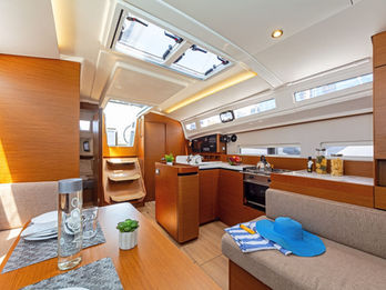 Jeanneau Sun Odyssey 410 interior saloon with U‑shaped seating and dining table, warm wood finish.