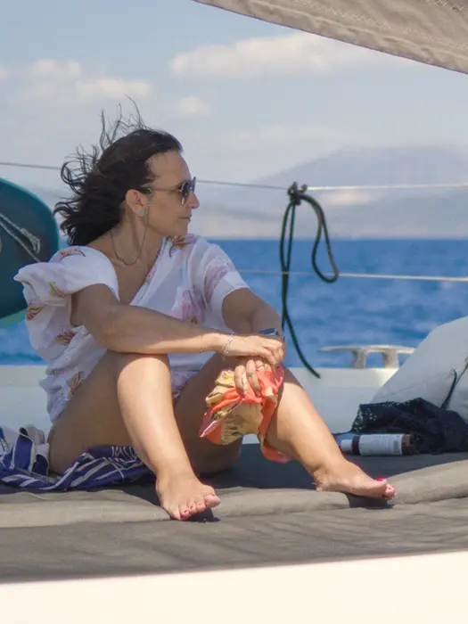 Woman relaxing on the bow of a catamaran, gazing ahead, enjoying the serenity of La Dolce Vita sailing experience in Greece.