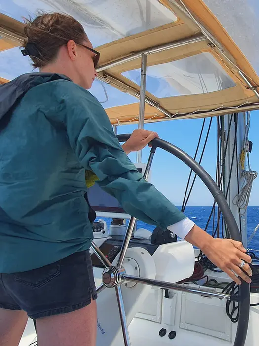 Woman focused at the helm, viewed slightly from behind, Catamaran Confidence training in Greece.