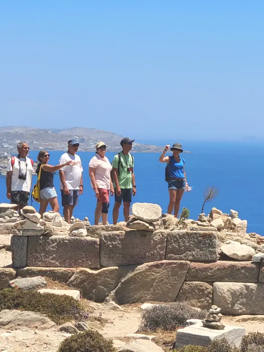 Epic Voyage group posing on sacred Delos island, ancient ruins and Aegean Sea in background.