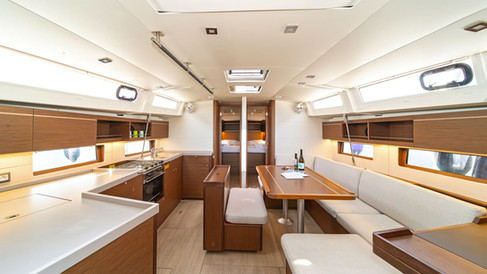 Monohull interior viewed from companionway, galley on one side, saloon seating and table beyond, functional and warm.
