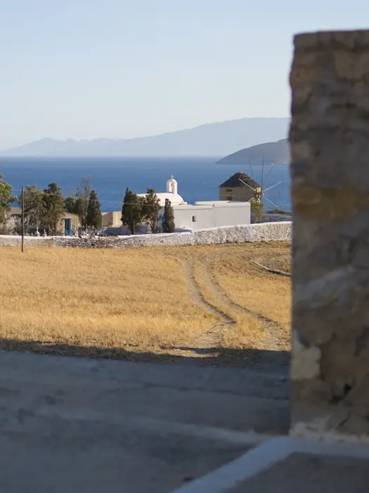 Yellow field, traditional church, blue Aegean with two distant islands, scenic view from Salty Fundamentals route.