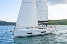 Aerial side view of a Dufour 470 monohull cutting through turquoise water under full sail.