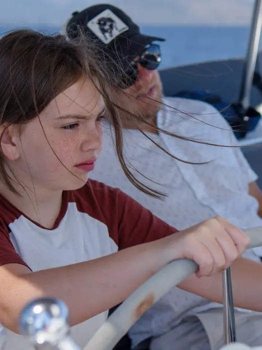 Young girl steering the boat beside her proud father, Family Holiday sailing moment.