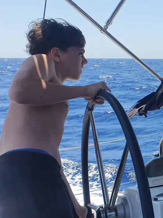 Young boy focused at the helm, learning to steer, Family Holiday sailing adventure in Greece.