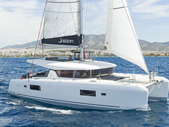 Lagoon 42 sailing toward the camera under full sails, aerial forward view, turquoise Aegean waters.