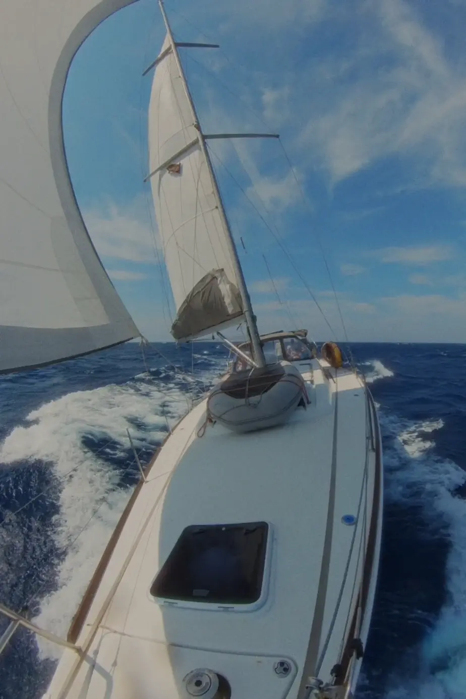 Sailing yacht on port tack with full jib and reefed main sail, view from bow toward stern, with the beautiful Aegean Sea in the background.