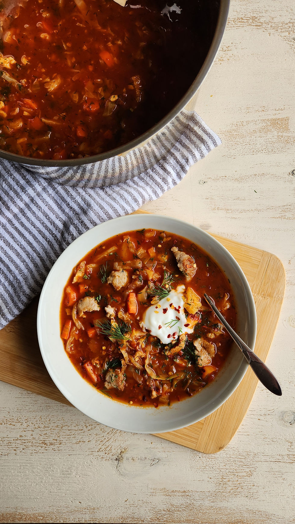A bowl of smokey turkey cabbage soup sitting next to the pot with theremaining soup