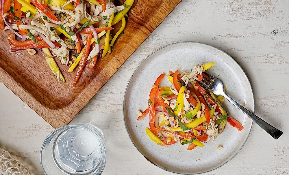 Square wood serving platting with Thai Chicken Mango Salad next to a smaller plate with Thai Chicken Mango Salad and a fork