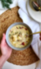 One hand holding the bowl of rustic potato dill soup and the other hand spooning the soup from the bowl as if they are about to eat it