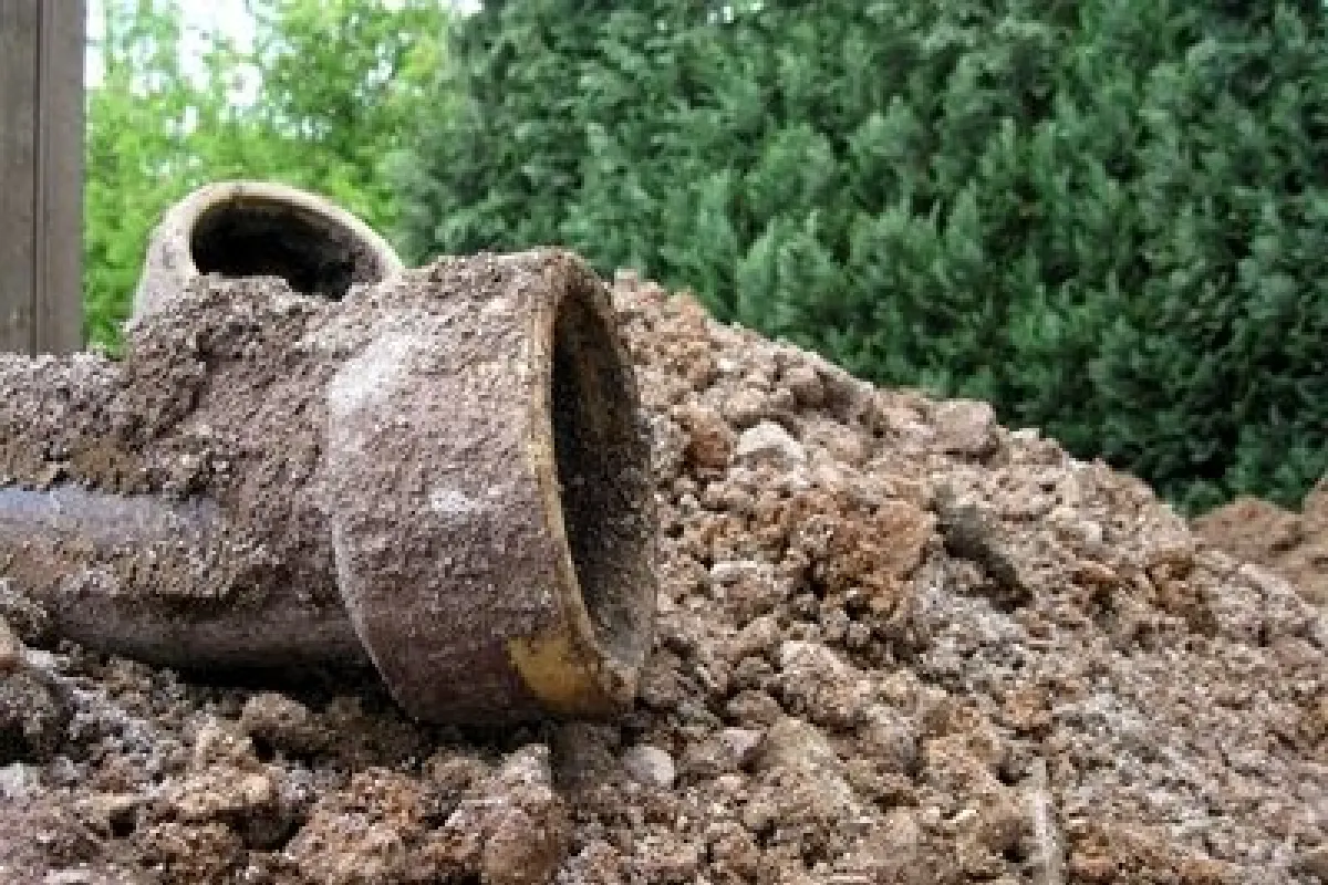 Image d'un tuyau de fosse septique cassé et abandonné sur un tas de terre, démontrant les risques de ne pas maintenir les systèmes d'assainissement