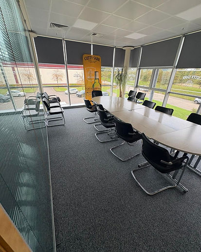 A modern conference room with a long, oval wooden table surrounded by black leather chairs
