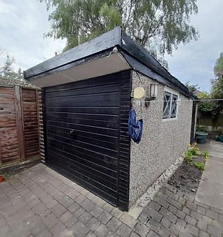 A detached pebble dashed garage featuring a black roller door alongside a paved driveway