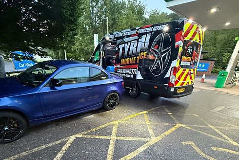 A blue car is parked in a gas station next to a "Tyres 4U" mobile service van
