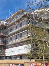 Large scale multi storey commercial building completely enclosed in scaffolding against a blue sky