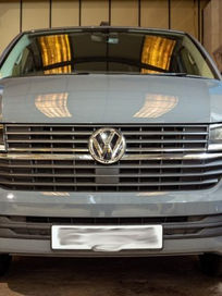 Front view of a grey Volkswagen Transporter van raised slightly on a workshop vehicle lift