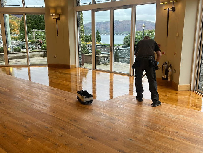 Worker applying finish to a wooden floor in a room with a scenic view and glass doors