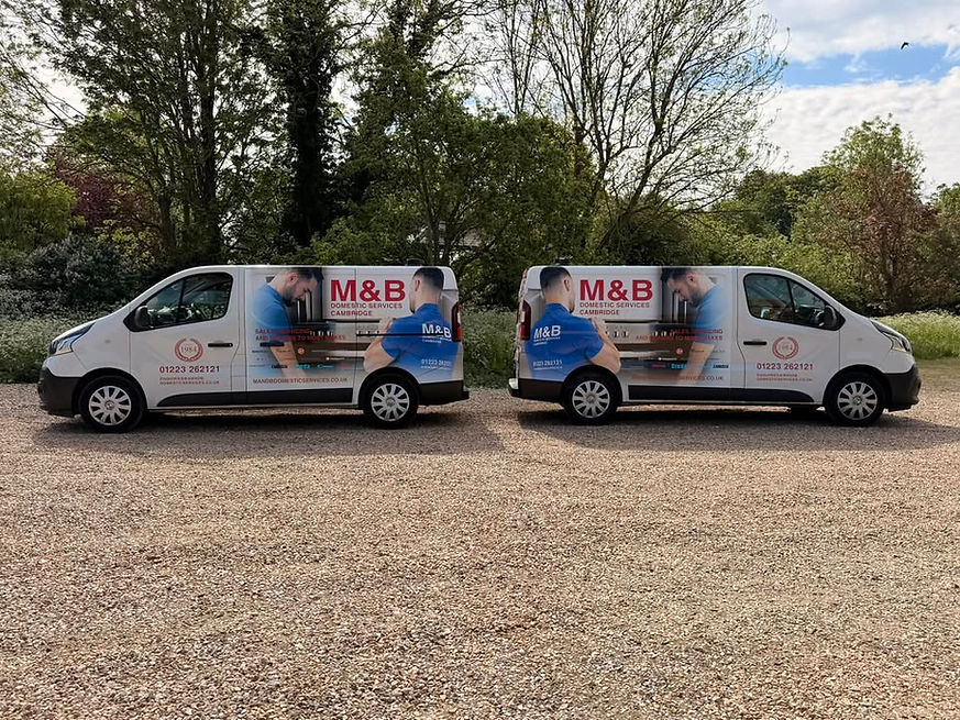 Two white vans with M&B branding are parked on a gravel surface
