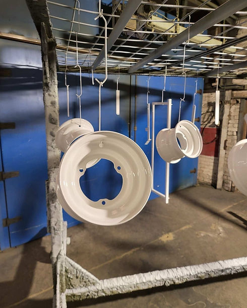 White painted vehicle wheel rims hanging from hooks on a drying rack