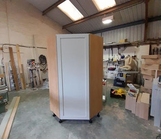 A tall wooden cabinet with white panel doors stands on a workshop floor