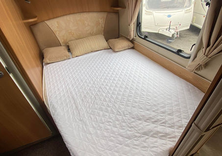 Fixed double bed in the rear of the caravan with overhead lockers