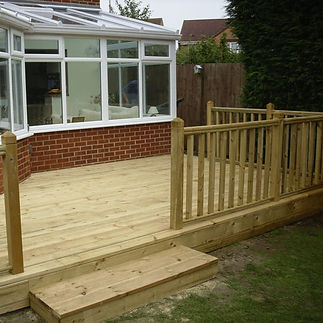 Wooden deck with railing adjacent to a brick house with a windowed sunroom