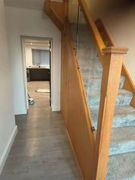 A narrow hallway with wooden stairs and glass railing on the right