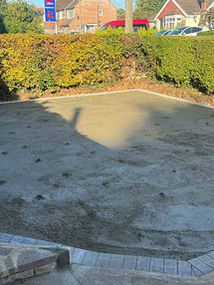 Prepared sub-base for a new driveway or patio area bordered by a low hedge and block paving