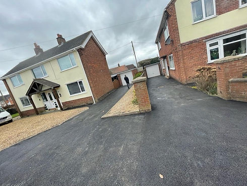 Tilted image of two brick houses with driveways, a person walking towards a garage