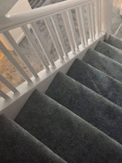 Winding domestic staircase fitted with dark grey carpet and white handrails