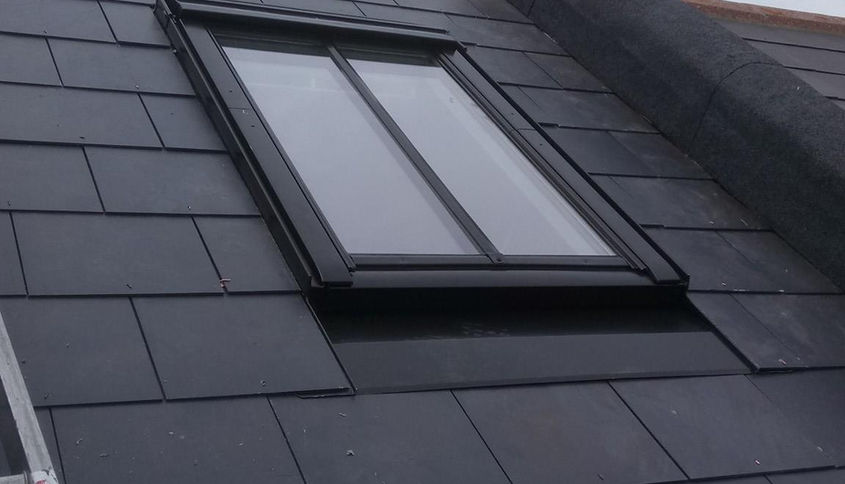 A rooftop with dark slate tiles features a closed rectangular skylight