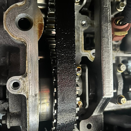 Close-up of a vehicle engine's inner workings, showing a black timing belt and silver gears