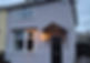 Small gray house facade with a black door under a wooden awning