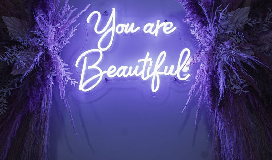 Glowing purple neon sign on a floral wall displaying the quote You are Beautiful