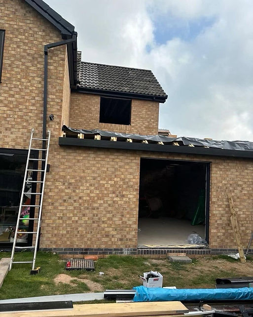An unfinished single-story brick extension under construction with exposed wooden roof