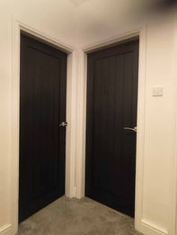 Two adjacent black paneled doors in a corner of a room with white walls 