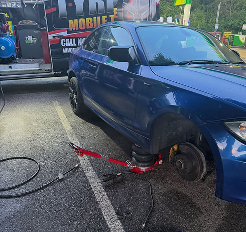 A blue car is jacked up in a service station, missing its front wheel