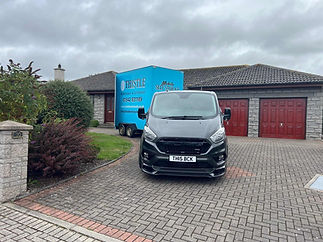 A grey van and a blue mobile self-storage trailer parked on a brick driveway