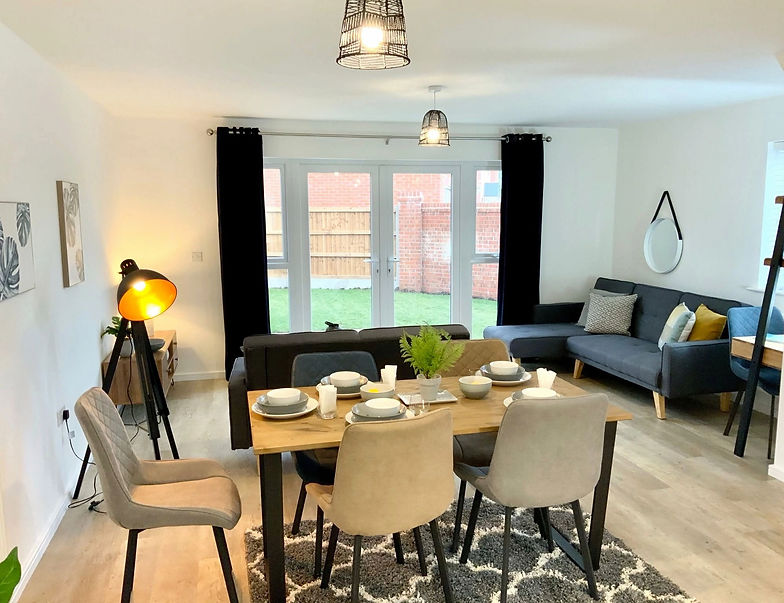 Staged living room area featuring a dark sofa, dining set, and oval wall mirror