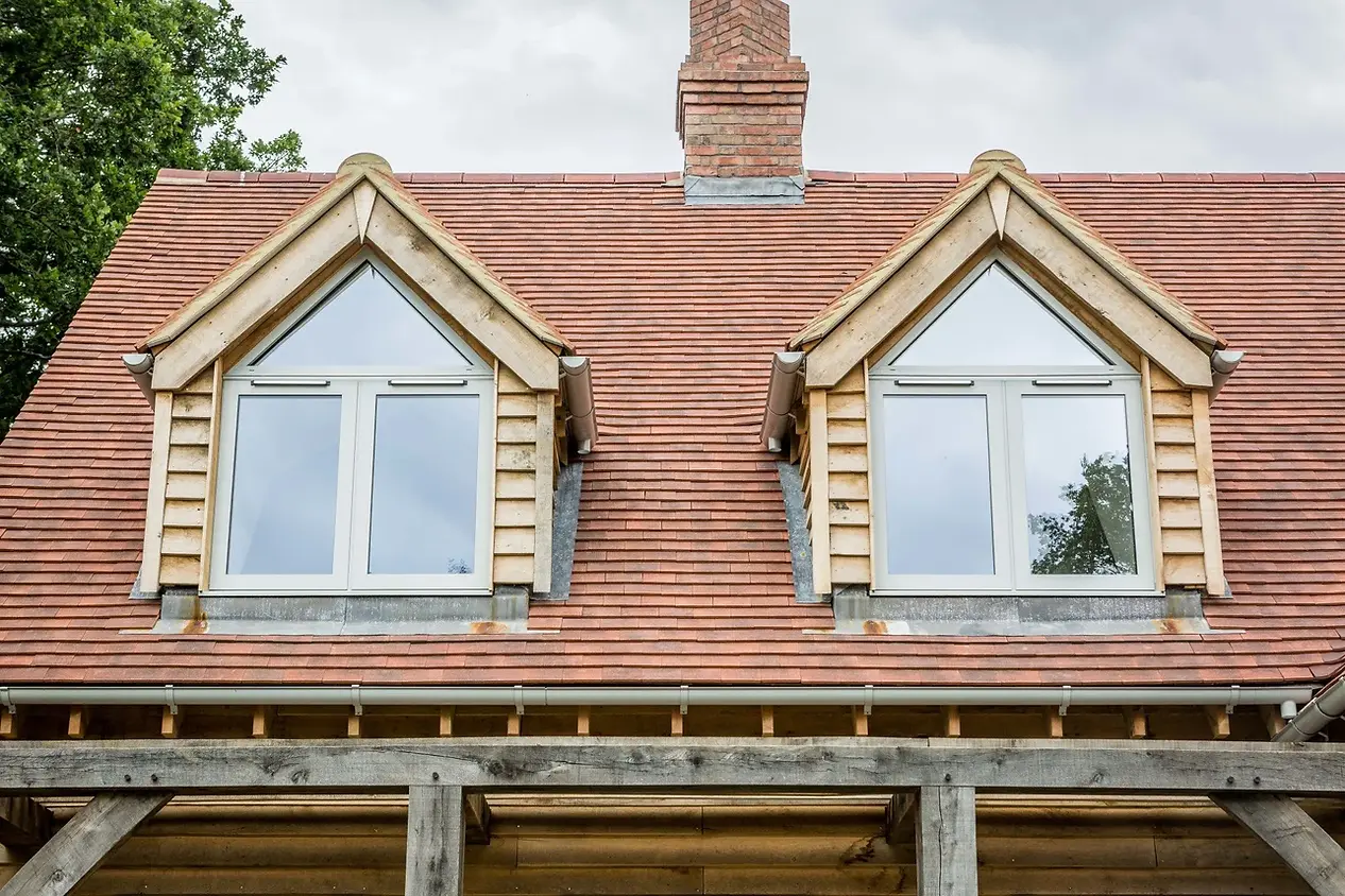 A wooden house with a red tile roof features two dormer windows 