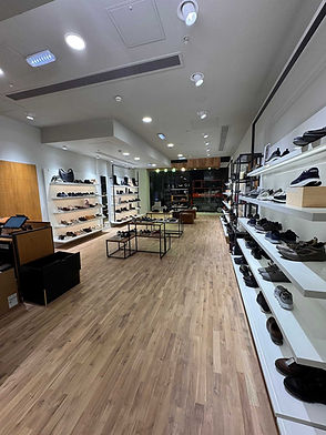 A modern shoe store with wooden flooring, featuring sleek white shelves displaying various shoes