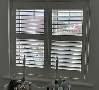 White plantation shutters cover a window, partially open to reveal a suburban view