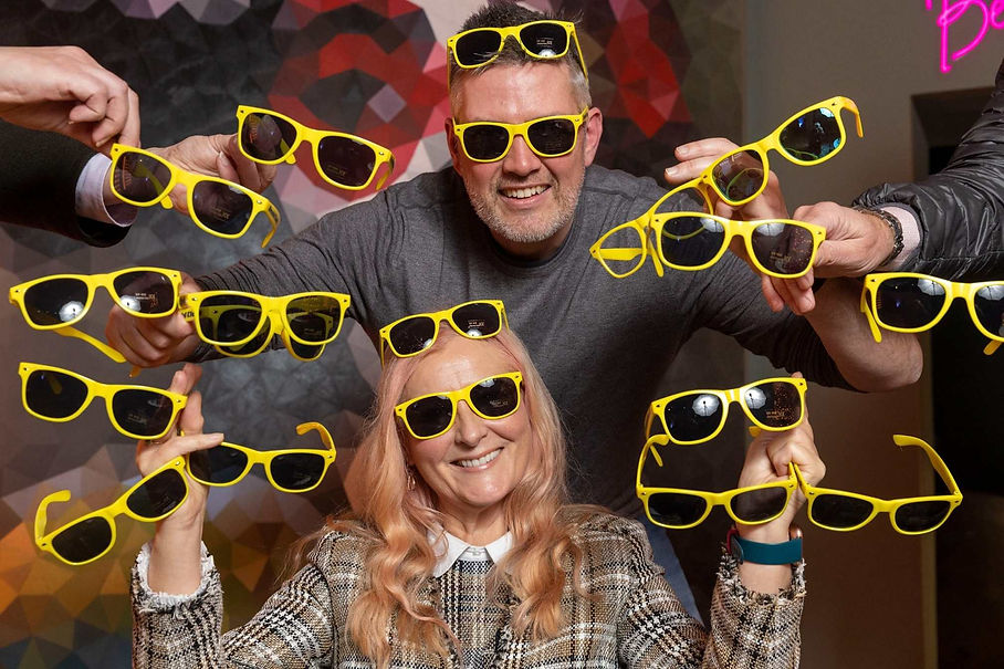 Smiling man and woman wearing and surrounded by bright yellow sunglasses