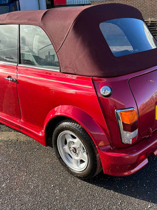 A classic red Mini Cooper convertible with a brown soft top is parked on a sunny day