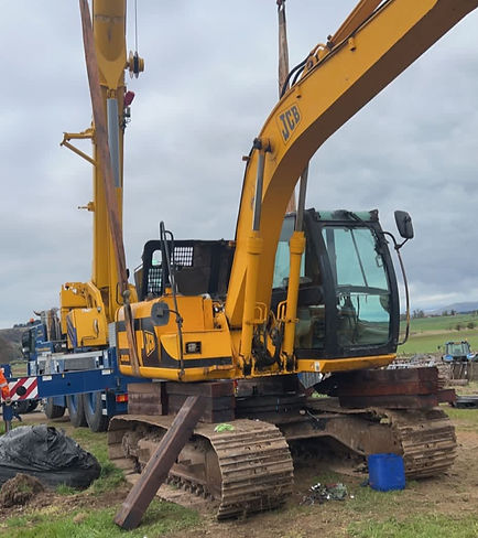 JCB excavator lifting a heavy steel beam with cable rigging on a construction site